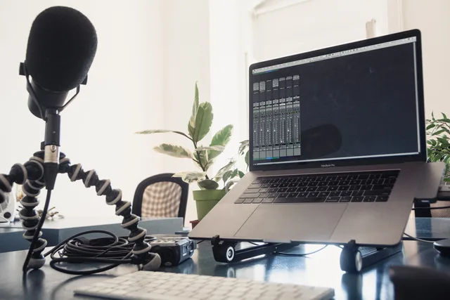 A detailed studio setup featuring a laptop and microphone on a desk for audio production. When to run podcast SEO benchmark research on your own numbers