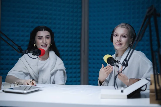 Two women podcasters engaging in discussion inside a modern recording studio with microphones. Before you build podcast SEO buyer personas, fix your data sources