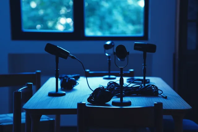 Dimly lit podcast studio with microphones and headphones on a table. What the ICO data protection fee means for podcast SEO budgets