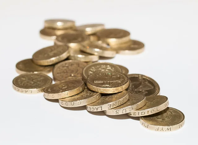 Close-up of assorted British pound coins scattered on a white surface, highlighting financial themes. Podcast SEO hidden costs explained for England budgets