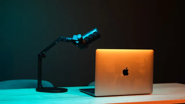Illuminated modern podcast setup with a microphone and laptop on a wooden desk. Nine steps to build a podcast SEO reporting dashboard