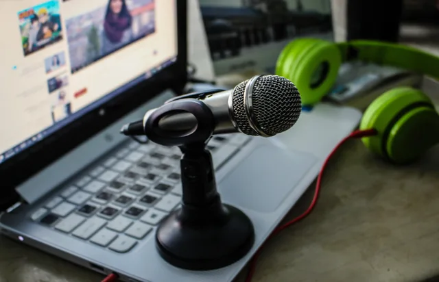 Close-up of a podcasting setup with a microphone, laptop, and green headphones. Scoring podcast SEO risks with a practical rubric