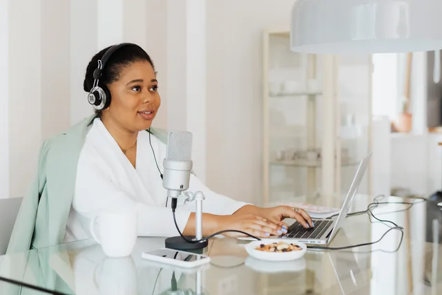 A woman working on a podcast in a modern home studio setup, using a laptop and microphone. What podcast SEO strategy mistakes mean for England's show discovery