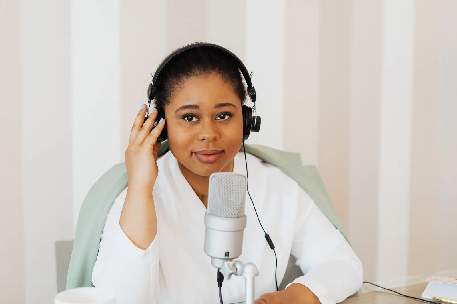 Young woman podcaster with headphones at a desk using a microphone.