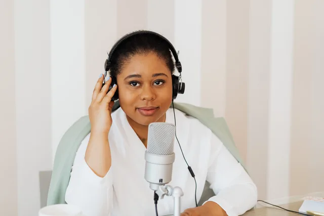 Young woman podcaster with headphones at a desk using a microphone. Why podcast SEO vendor due diligence starts with their data sources